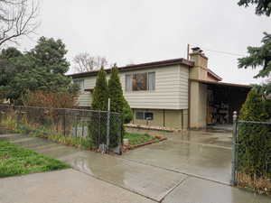 View of side of property featuring a chimney, concrete driveway, an attached carport, and a gate
