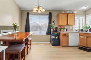 Kitchen featuring light countertops, white dishwasher, a chandelier, light wood finished floors, and decorative light fixtures