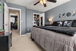 Bedroom with a spacious closet, light colored carpet, and ceiling fan