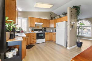 Kitchen with light countertops, freestanding refrigerator, electric stove, light wood-style flooring, and vaulted ceiling