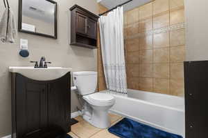 Full bathroom featuring vanity, shower / tub combo with curtain, tile patterned floors, and a textured wall