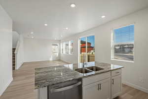 **DISCALIMER** Interior options may vary.Kitchen with light stone counters, white cabinetry, stainless steel dishwasher, a center island with sink, and light wood-style flooring
