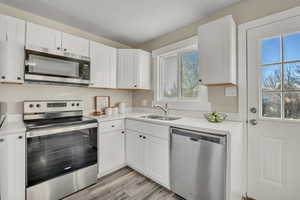 Kitchen with appliances with stainless steel finishes, white cabinets, and light wood-style flooring