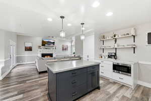 Kitchen featuring pendant lighting, white cabinets, recessed lighting, a warm lit fireplace, and stainless steel microwave