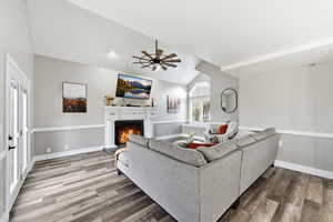 Living area featuring lofted ceiling, a lit fireplace, wood finished floors, and ceiling fan