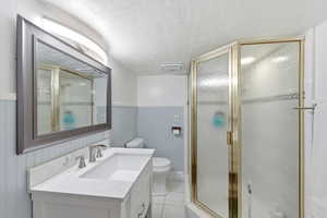 Bathroom featuring a textured ceiling, wainscoting, vanity, a shower stall, and light tile patterned floors