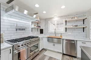 Kitchen featuring open shelves, stainless steel appliances, light stone countertops, wall chimney exhaust hood, and tasteful backsplash