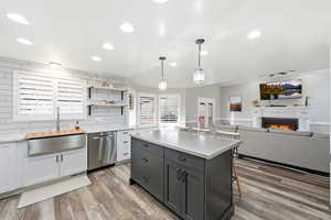 Kitchen with a breakfast bar, pendant lighting, white cabinetry, a warm lit fireplace, and decorative backsplash