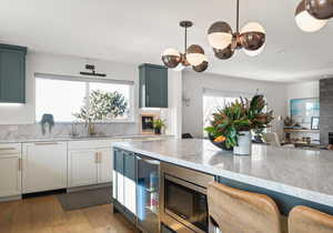 Kitchen featuring light stone counters, stainless steel microwave, light wood finished floors, beverage cooler, and paneled dishwasher