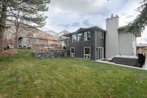 Rear view of property featuring board and batten siding, a chimney, a hot tub, a mountain view, and a patio area