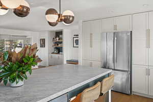 Kitchen featuring freestanding refrigerator, light countertops, white cabinets, light wood-type flooring, and a breakfast bar