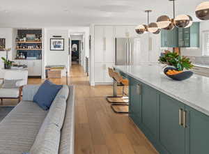 Kitchen with green cabinets, light wood-style floors, glass insert cabinets, marble counters, and white cabinetry