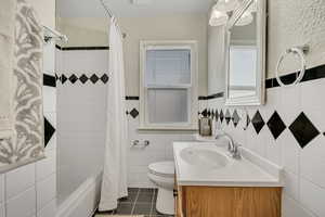 Bathroom with shower / tub combo with curtain, vanity, tile walls, wainscoting, and dark tile patterned flooring
