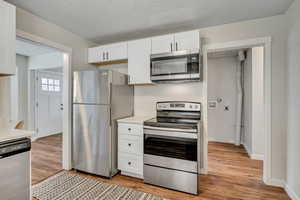 Kitchen featuring stainless steel appliances, white cabinets, light wood-style flooring, and a textured ceiling