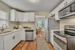Kitchen featuring stainless steel appliances, white cabinetry, a textured ceiling, light wood-type flooring, and light stone counters