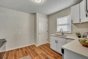 Kitchen featuring white cabinets, light wood-style floors, a textured ceiling, light stone counters, and stainless steel electric stove
