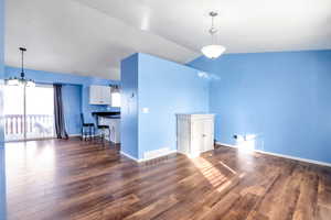 Unfurnished living room featuring dark wood-style flooring, a chandelier, and lofted ceiling