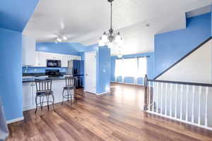 Kitchen featuring dark countertops, white cabinets, a chandelier, dark wood-style floors, and black appliances