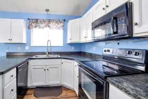 Kitchen with black appliances, dark countertops, white cabinets, and hanging light fixtures