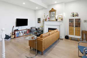 Living area featuring light wood finished floors, a tiled fireplace, beamed ceiling, and recessed lighting