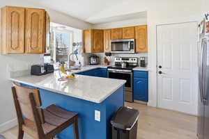 Kitchen featuring light stone countertops, stainless steel appliances, blue cabinetry, a peninsula, and lofted ceiling