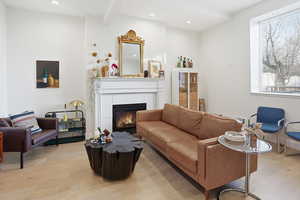 Living room with beamed ceiling, a fireplace, light wood finished floors, and recessed lighting