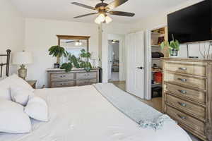 Bedroom with ceiling fan, a walk in closet, and light carpet