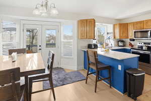 Kitchen with appliances with stainless steel finishes, blue cabinets, light stone counters, decorative light fixtures, and light wood-style flooring