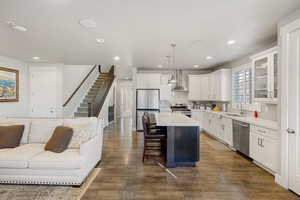 Kitchen featuring open floor plan, glass insert cabinets, white cabinets, a kitchen island, and decorative light fixtures