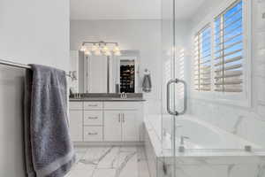 Full bathroom featuring double vanity, a garden tub, light marble finish flooring, and a shower with door