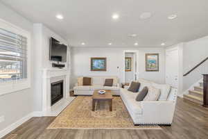Living area with a glass covered fireplace, wood finished floors, recessed lighting, and stairs