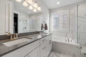 Full bath with double vanity, a marble finish shower, light marble finish flooring, a bath, and a spacious closet