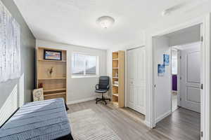 Bedroom with light wood-style flooring, a textured ceiling, a closet, and an office area
