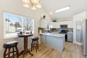 Kitchen featuring a peninsula, appliances with stainless steel finishes, light countertops, tasteful backsplash, and high vaulted ceiling