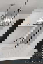 Kitchen with hanging light fixtures, light stone counters, a kitchen island with sink, and dark cabinetry