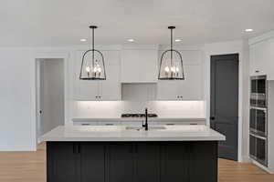 Dual tone kitchen featuring hanging lights, decorative backsplash, a center island with sink, two tone color scheme, and light stone counters