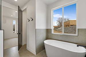 Full bathroom with tile walls, a freestanding tub, light tile patterned floors, a wainscoted wall, and recessed lighting