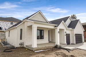 View of front of property featuring covered porch, roof with shingles, brick siding, an attached garage, and driveway
