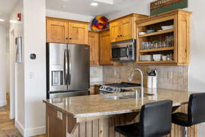 Kitchen featuring appliances with stainless steel finishes, a kitchen bar, backsplash, light stone counters, and recessed lighting