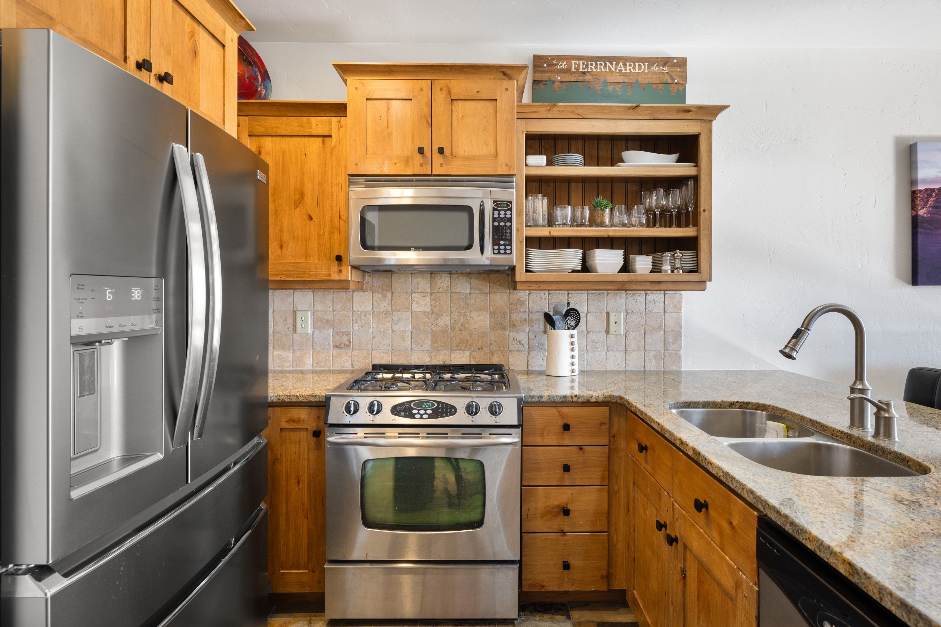 Kitchen with appliances with stainless steel finishes, light stone counters, open shelves, brown cabinetry, and backsplash
