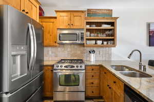 Kitchen with appliances with stainless steel finishes, light stone counters, open shelves, brown cabinetry, and backsplash