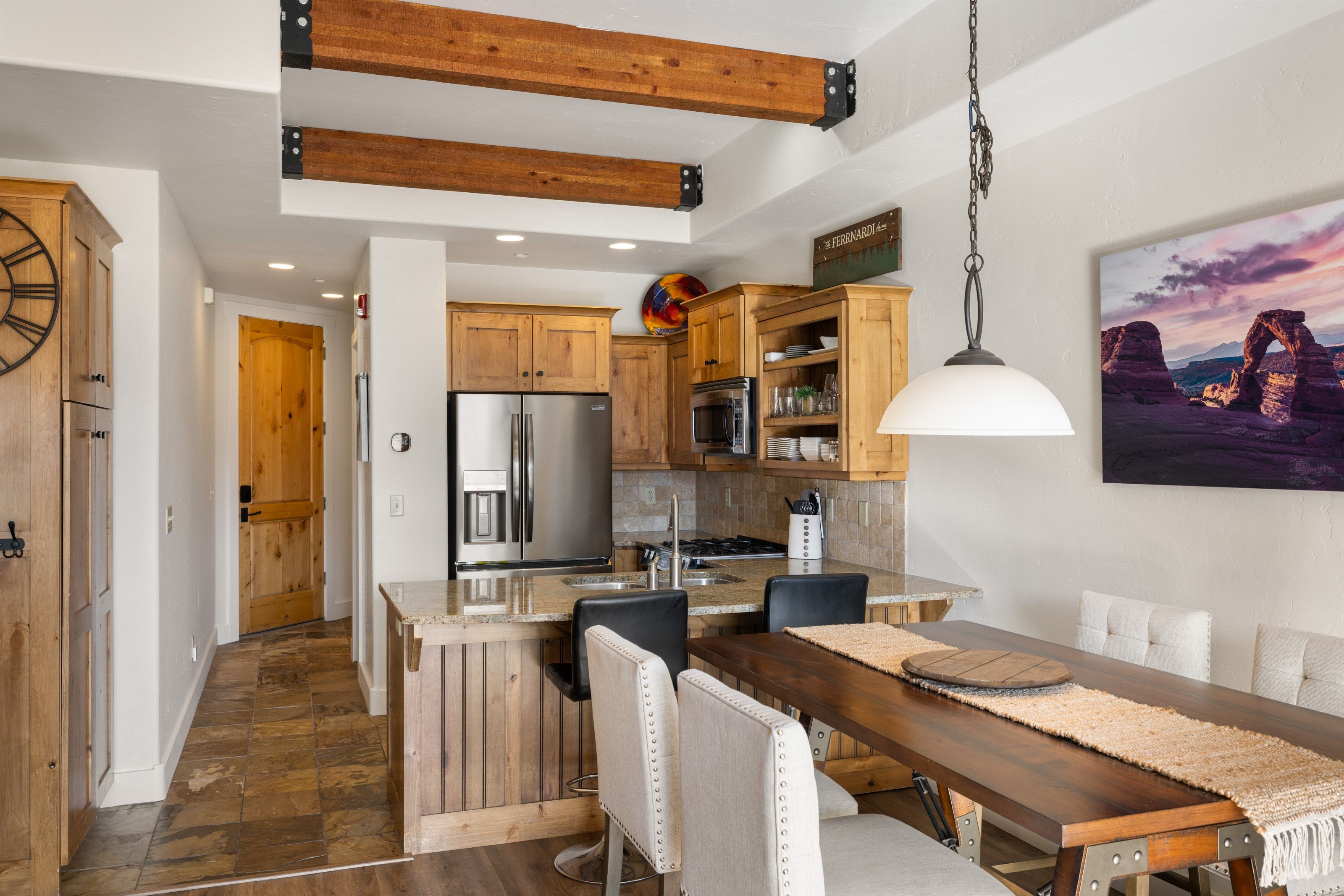 Kitchen featuring a peninsula, light stone counters, decorative light fixtures, appliances with stainless steel finishes, and brown cabinetry