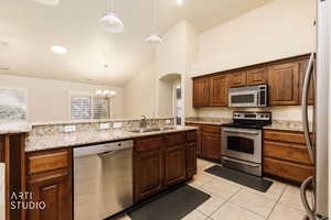 Kitchen featuring appliances with stainless steel finishes, hanging light fixtures, a chandelier, light stone countertops, and high vaulted ceiling