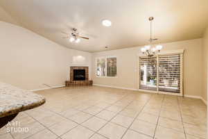 Unfurnished living room featuring ceiling fan, light tile patterned flooring, a tile fireplace, vaulted ceiling, and a chandelier