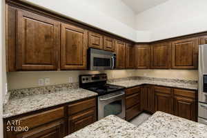Kitchen featuring stainless steel appliances, light stone countertops, and dark brown cabinets