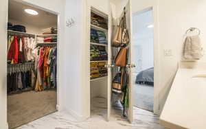 Walk in closet featuring light marble finish flooring and light carpet