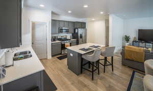 Kitchen featuring open floor plan, a center island, appliances with stainless steel finishes, light wood-type flooring, and gray cabinets