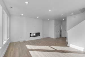 Unfurnished living room featuring a glass covered fireplace, recessed lighting, and light wood finished floors