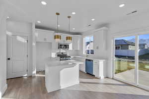 Kitchen with appliances with stainless steel finishes, pendant lighting, white cabinetry, a center island, and light wood-style floors
