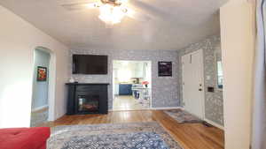 Living area featuring a textured ceiling, light wood-style floors, a glass covered fireplace, arched walkways, and ceiling fan